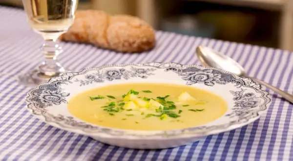 Eine cremige Zucchini-Suppe mit frischer Petersilie in einer eleganten Schüssel, daneben ein Glas Weißwein und ein Brot.