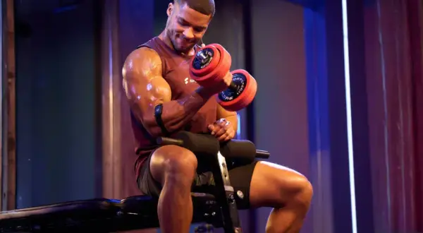 Mann mit Hantel beim Fitness-Training. Schweißglänzende Muskeln, konzentrierter Blick.