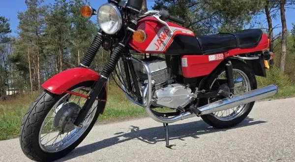 Czerwona Jawa TS 350, jeden z kultowych motocykli, gotowa na przejażdżkę po leśnej drodze.