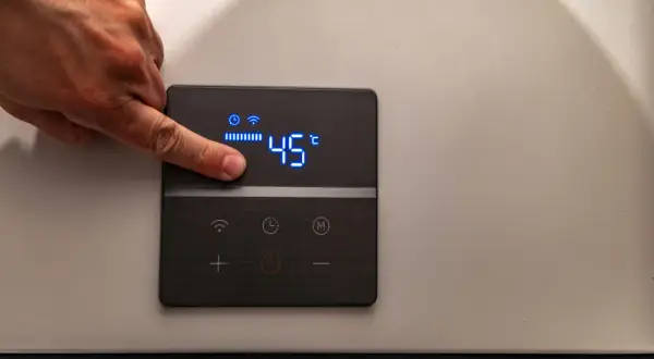 Dito un dito regola la temperatura di 45°C su un pannello di controllo di caldaie elettriche per riscaldamento.
