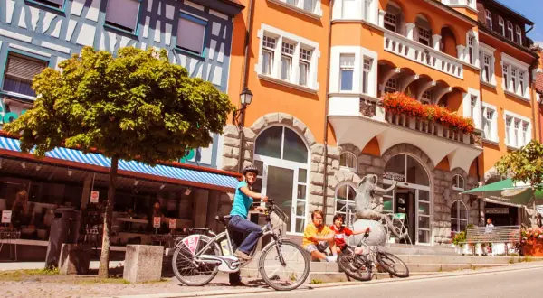 Familie genießt sonnigen Tag in der Stockach Altstadt. Kinder sitzen auf Treppen, Mutter auf Fahrrad.