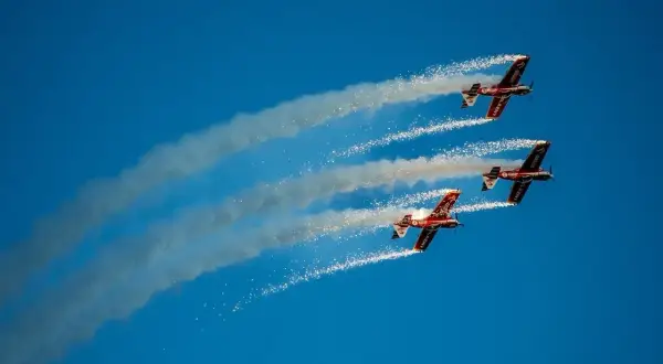 Trzy samoloty akrobacyjne w formacji, wypuszczające dym i iskry na błękitnym niebie. Niezapomniane wrażenia z kiedy air show w Radomiu.