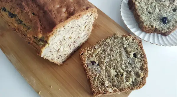 Domowy chlebek bananowy z kawałkami orzechów i rodzynek, pokrojony na desce.