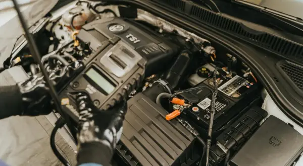 Mechanik w rękawiczkach sprawdza czujnik położenia wału za pomocą testera diagnostycznego podłączonego do akumulatora.