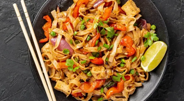 Pyszny pad thai z kurczakiem, makaronem ryżowym, warzywami i limonką.