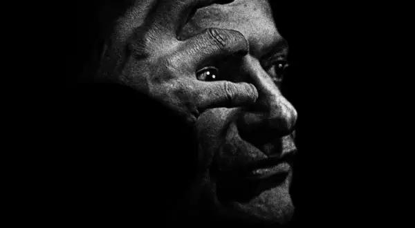 Intensywny portret w czerni i bieli, gdzie dłoń zakrywa oko, przywołuje mroczny styl antoine d'agata.