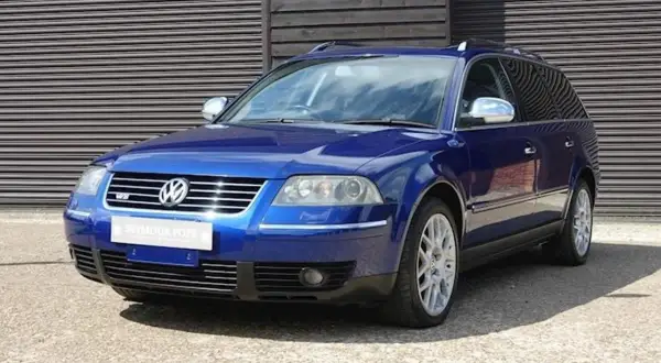 En blå Passat W8 kombi står parkerad framför en träfasad.