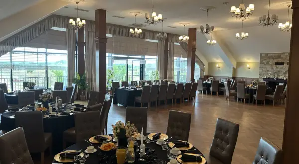 Elegancka sala bankietowa w ośrodku jeździeckim Lando, przygotowana na przyjęcie. Stoły nakryte czarnymi obrusami, złote talerze i eleganckie krzesła.