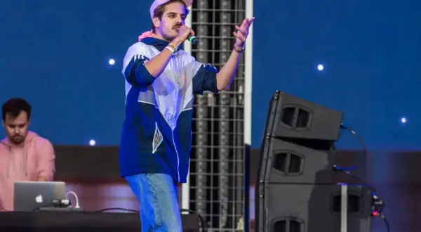 Artysta na scenie, jeden z najpopularniejszych polskich wykonawców pop, śpiewa do mikrofonu. W tle DJ przy laptopie.