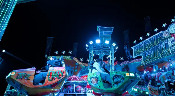 Bunte Fahrgeschäfte und Lichter auf dem Berliner Volksfest. Menschen genießen die Nacht auf dem "Break Dance".