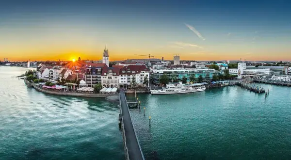Friedrichshafen heute: Sonnenuntergang über dem Bodensee, mit Schiffen im Hafen und der Promenade.