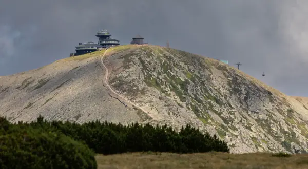 Kamienna ścieżka prowadzi na szczyt Śnieżki, gdzie widać budynki obserwatorium i kolejkę linową.