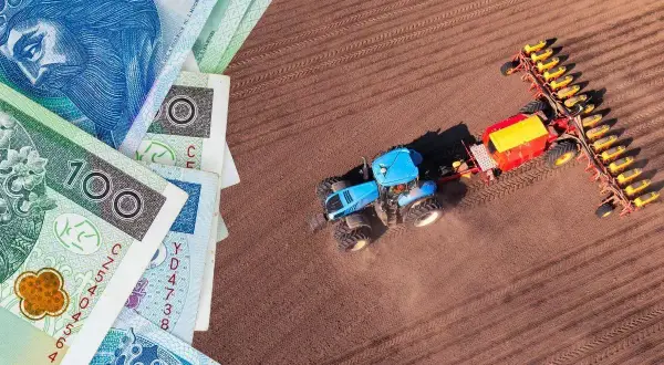 Pieniądze i niebieski traktor z siewnikiem na polu. Czy to symbol rolnictwa i podatku rolnego?