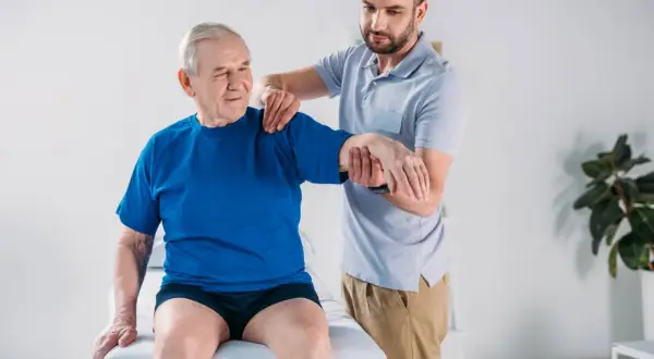 Fisioterapista assiste un anziano con debolezza muscolare, valutando la mobilità del braccio.