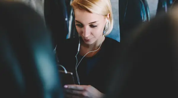 Kobieta w słuchawkach korzysta z telefonu, ciesząc się internetem w samolocie.