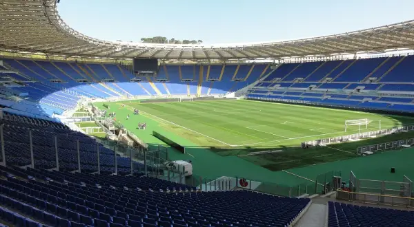 Puste trybuny stadionu Lazio, z zieloną murawą i bramkami, czekają na kibiców.