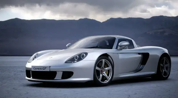 Srebrny Porsche Carrera GT na pustkowiu, z górami w tle.