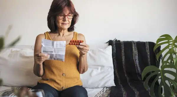 Kobieta czyta ulotkę leku, trzymając opakowanie tabletek. Szuka informacji o lekach na menopauzę bez recepty.
