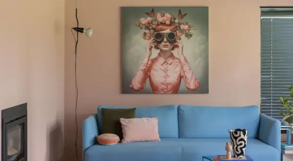 Peinture pièce de vie : un tableau surréaliste d'une femme aux lunettes et couronnes de fruits, sur un canapé bleu vif.