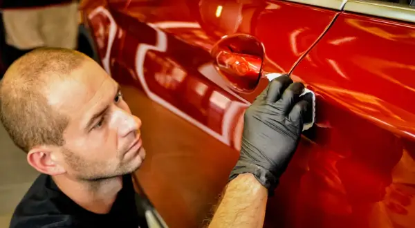 Detailer nakłada powłokę kwarcową czy ceramiczną na błyszczący, czerwony lakier samochodu, dbając o każdy detal.