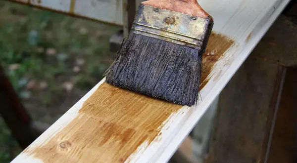 Application d'une lasure blanche sur une planche de bois. Le résultat avant/après est visible sur la surface traitée.