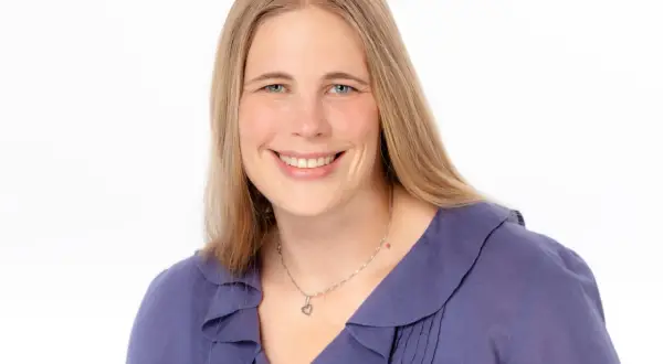 Lächelnde Frau mit blonden Haaren und blauen Augen, trägt eine lila Bluse. Sie könnte eine engagierte studentische Hilfskraft sein.