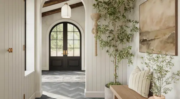 A bright, airy hallway with a dark arched doorway leading outside. A potted tree and bench add warmth to the space.