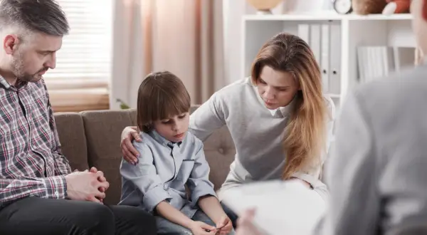 Rodzina na terapii. Matka wspiera syna, ojciec zamyślony. Sesja terapeutyczna w nurcie psychodynamicznym.