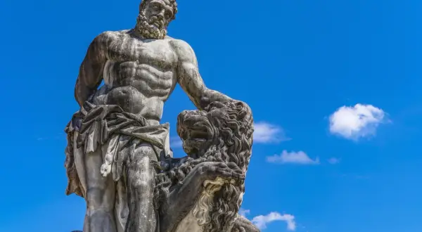 Statue de marbre d'Hercule, dieu grec, luttant contre un lion, sous un ciel bleu éclatant.