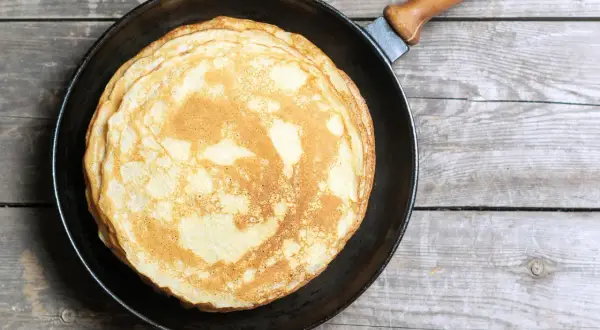 Ein Stapel goldbrauner, veganer Pfannkuchen liegt in einer Pfanne auf rustikalem Holz.