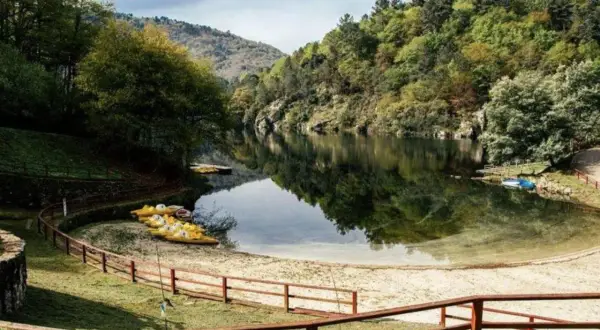 Playa fluvial a Calzada con kayaks amarillos esperando en la arena, rodeada de árboles verdes y un río tranquilo.