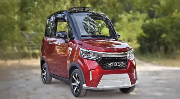 Auto rossa compatta, ideale per la mobilità ridotta, con tetto apribile e dettagli moderni, parcheggiata su una strada sterrata tra gli alberi.