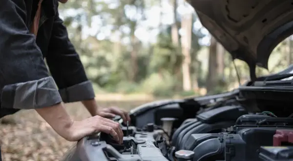 Un homme regarde le moteur de sa voiture qui cale à bas régime, bloqué en pleine nature.