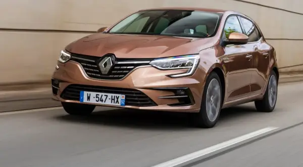 Brązowy Renault Megane RS 4 pędzi po drodze, jego reflektory ostro świecą.