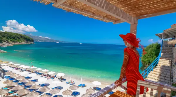 Kobieta w czerwonej sukience podziwia turkusowe morze i plażę z leżakami. Idealne miejsce, by sprawdzić, gdzie najtaniej na wakacje.