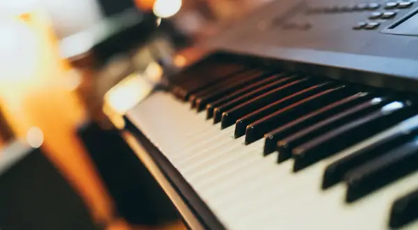 Klawiatura keyboardu, gotowa do zagrania popularnych piosenek. Ciepłe światło otoczenia tworzy przytulną atmosferę.