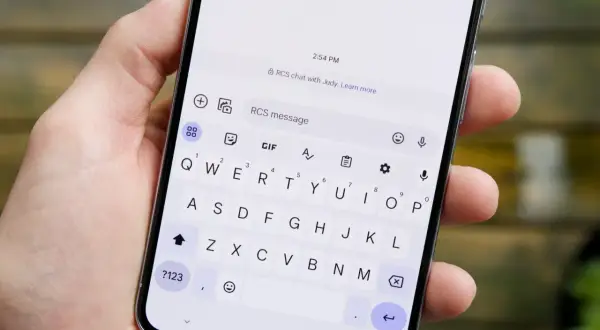 Dłoń trzyma smartfon z otwartą klawiaturą. Na ekranie widać informację "RCS chat with Judy", co wyjaśnia, rcs co to jest.