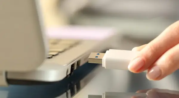 Dłoń wkłada biały pendrive do portu USB laptopa, rozpoczynając nagrywanie danych.