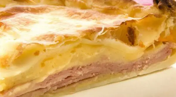 Rebanada de tarta de jamón y queso, con capas de masa dorada, jamón rosado y relleno cremoso. ¡Un bocado delicioso!
