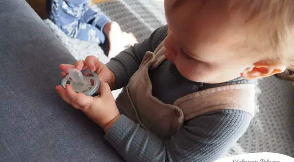 Dziecko bawi się smoczkiem, co może być pierwszym krokiem, jak odzwyczaić dziecko od smoczka.