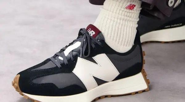 Sznurowanie butów New Balance. Ciemne sneakersy z białym logo N i brązową podeszwą.