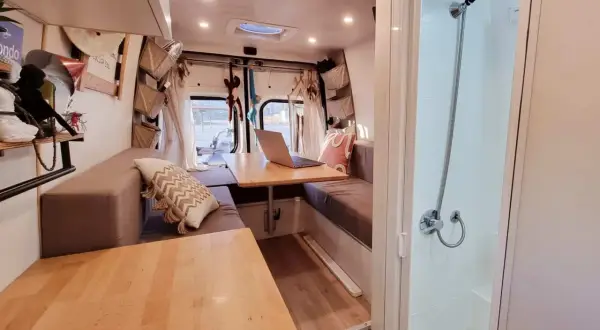 Interno camper con divanetti, tavolo e un box doccia in legno fai da te.