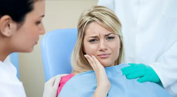 Kobieta cierpi na ból zęba po zatruciu. Dentysta i asystentka próbują jej pomóc.