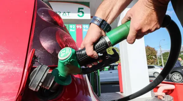 Remplissage d'une voiture thermique rouge à la station-service. Le pistolet vert est inséré dans le réservoir.
