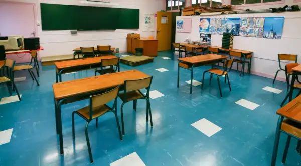 Pusta klasa szkolna z rzędami drewnianych ławek i krzeseł na niebieskiej podłodze.