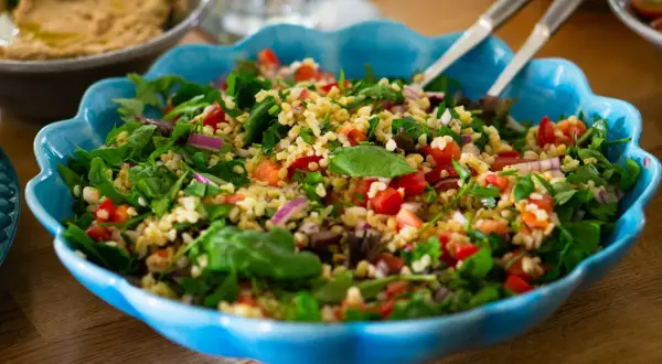 En stor blå skål fylld med ett färgglatt tabbouleh recept med bulgur, tomater, lök och färska örter.