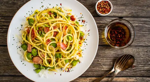 Pyszny makaron z bobem, chrupiącym boczkiem i parmezanem, podany z oliwą i płatkami chili. Idealny na szybki obiad.