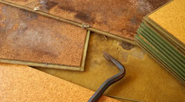 Beschädigter Laminatboden mit deutlichen Wasserflecken und einem Brecheisen. Die Korkunterlage ist aufgeweicht.