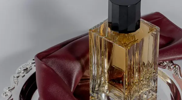 Eleganckie perfumy z lat 2000. w szklanej butelce z czarną nakrętką, na ozdobnej tacy z bordową skórką.