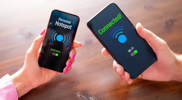 Dwie dłonie trzymają telefony. Na jednym ekranie "Personal Hotspot Activated...", na drugim "Connected! Wi-Fi".